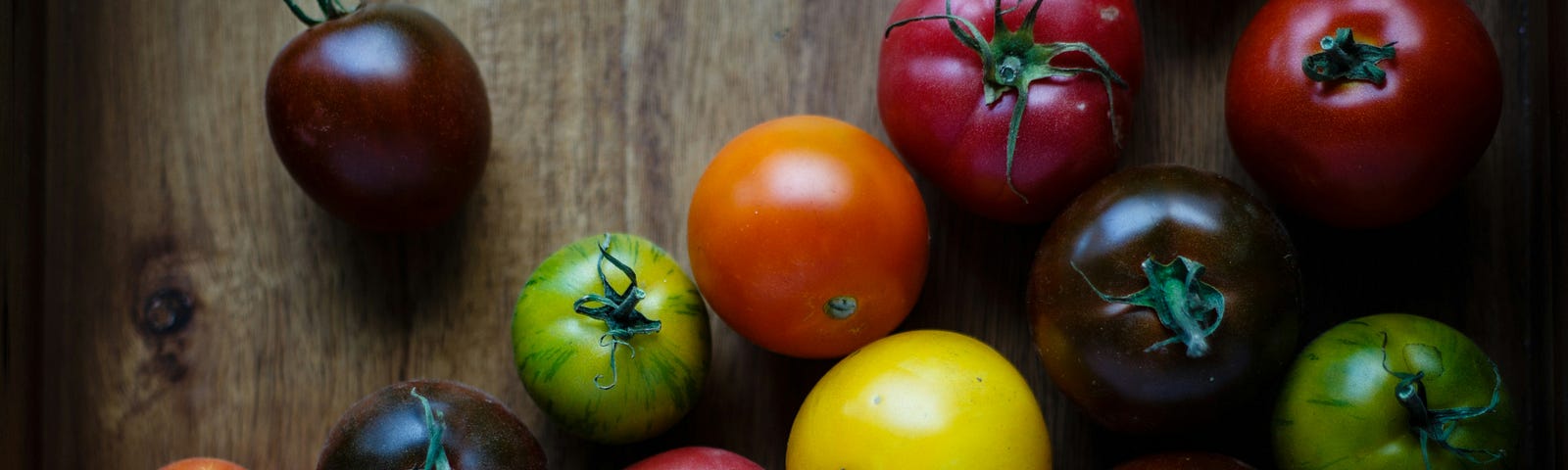 Multiple varieties of tomato, of varying and vibrant colors, are on a wooden table.