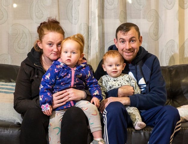 A man and a woman sat in a sofa each of them holding a toddler.