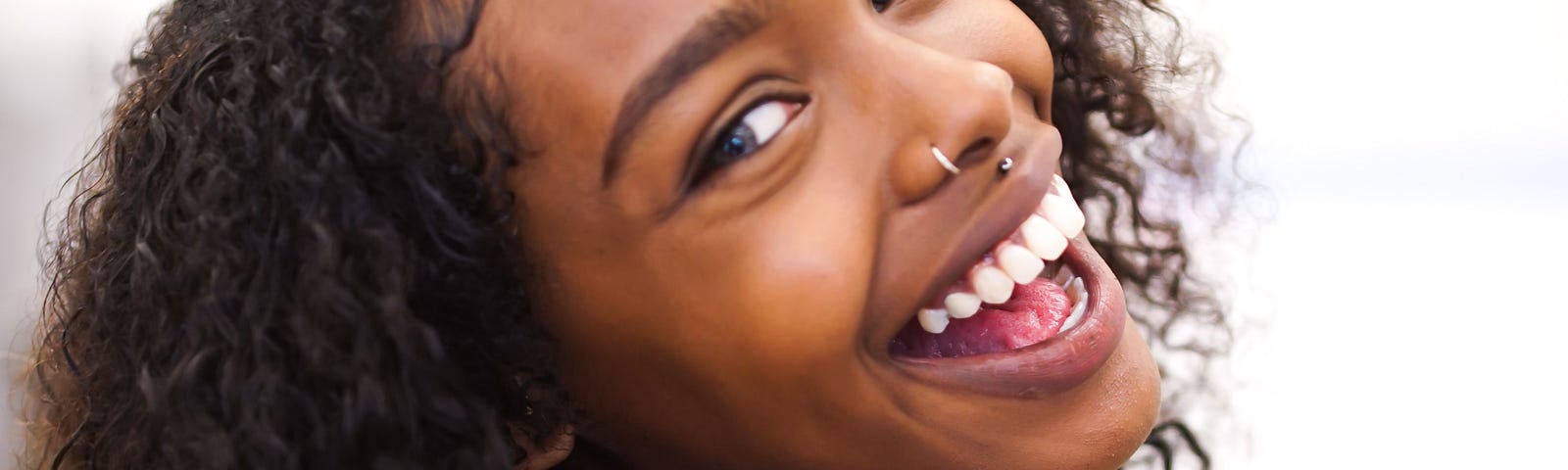 The big smile and happy eyes, curly hair and happy face of a young girl.