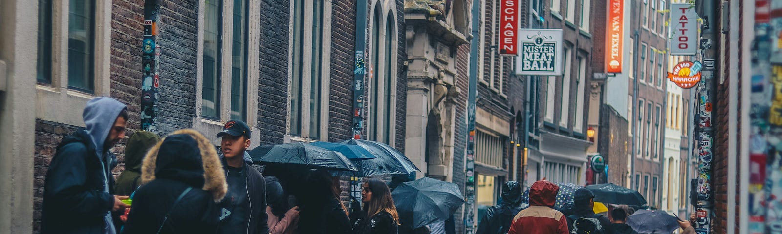 People crowded together on a narrow street with umbrellas.