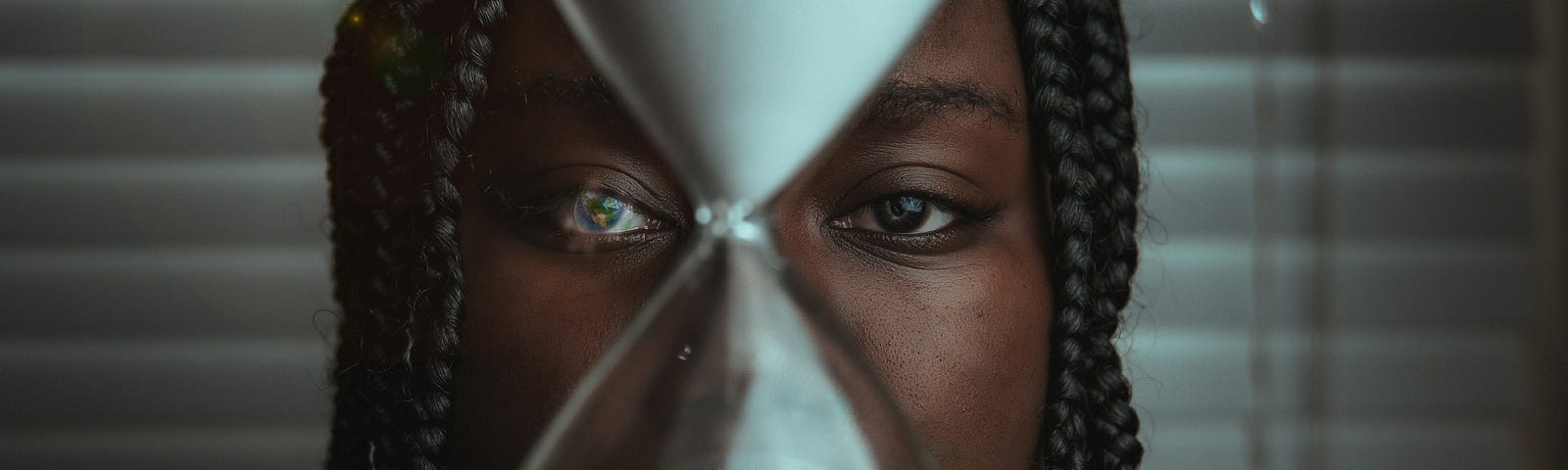 A black woman holding an hour glass in front of her face.