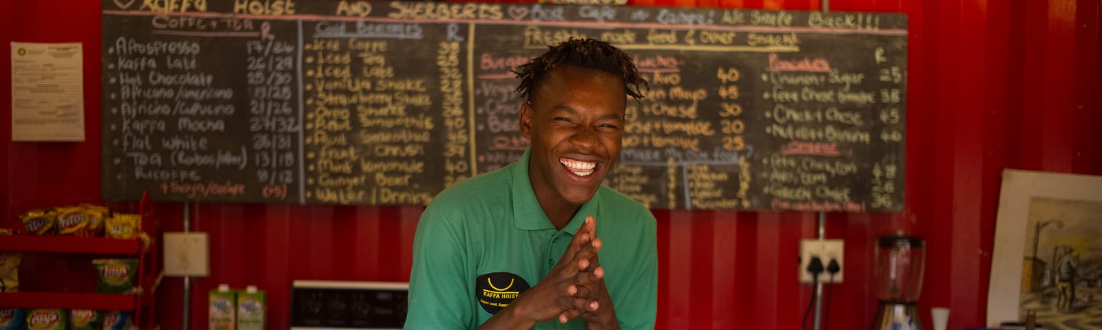 A very happy young man, with the cutest smile in the world, behind a sandwich counter, ready to take your order.