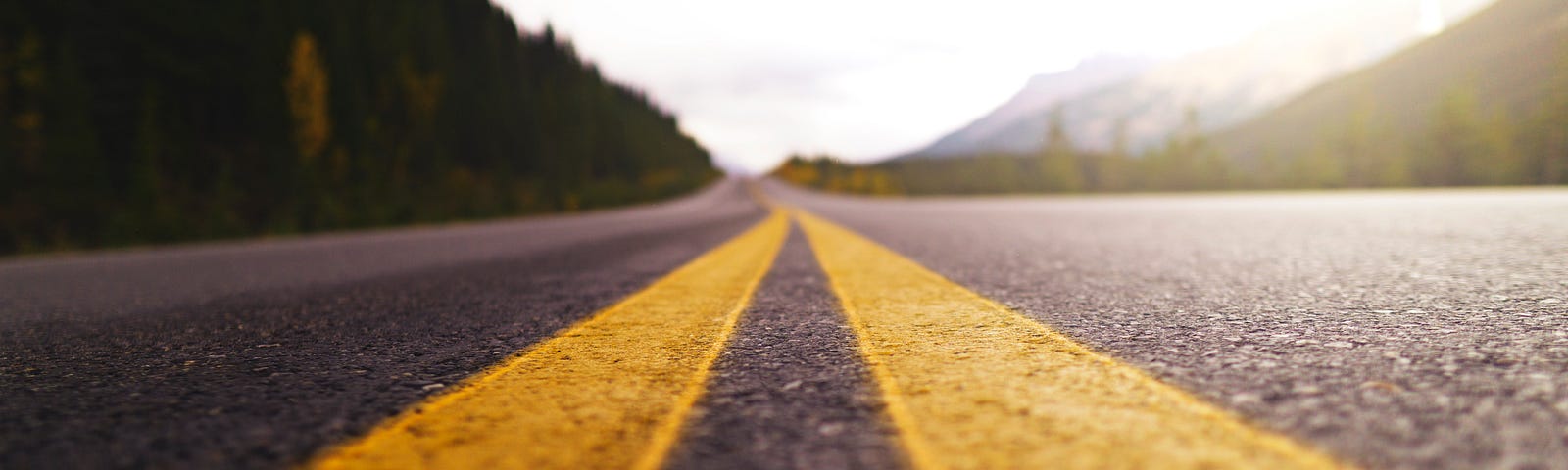 A two-lane highway with double-yellow line painted down the center; trailing into the distance.