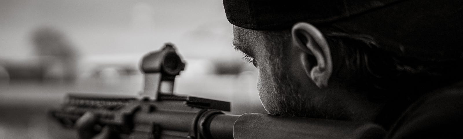 Black and white photo of man pointing an assault rifle.