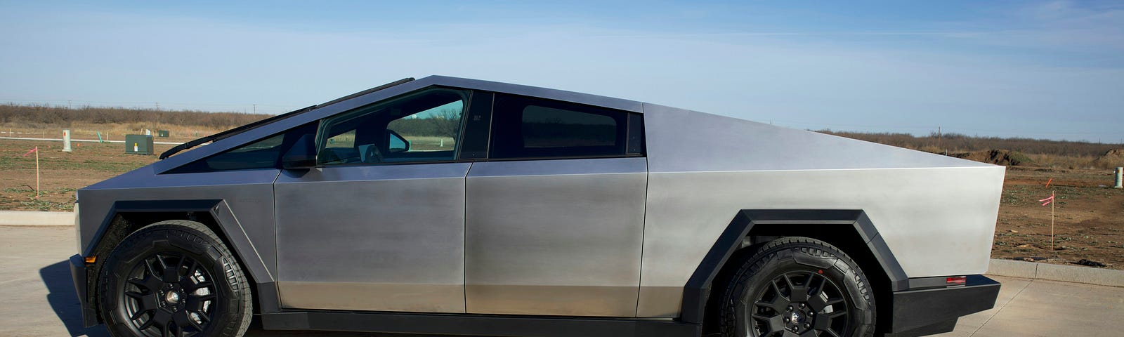 Photo of a steel grey Cybertruck sitting on concrete.