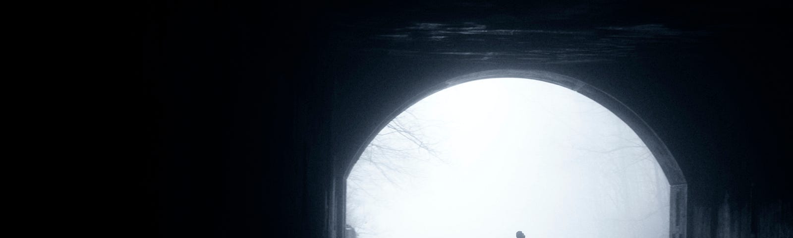 Black and white photo of a figure entering a dark tunnel.