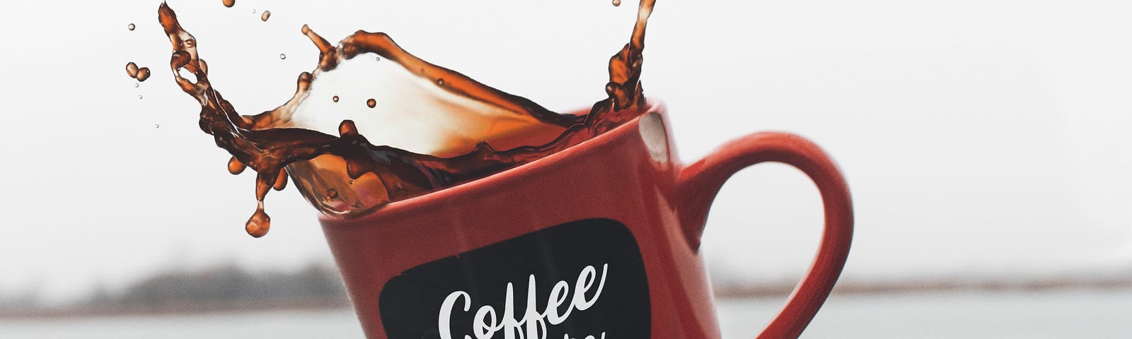 A right outstretched hand tosses a coffee cup into the air, with the coffee splashing upwards. Lake water in the background.