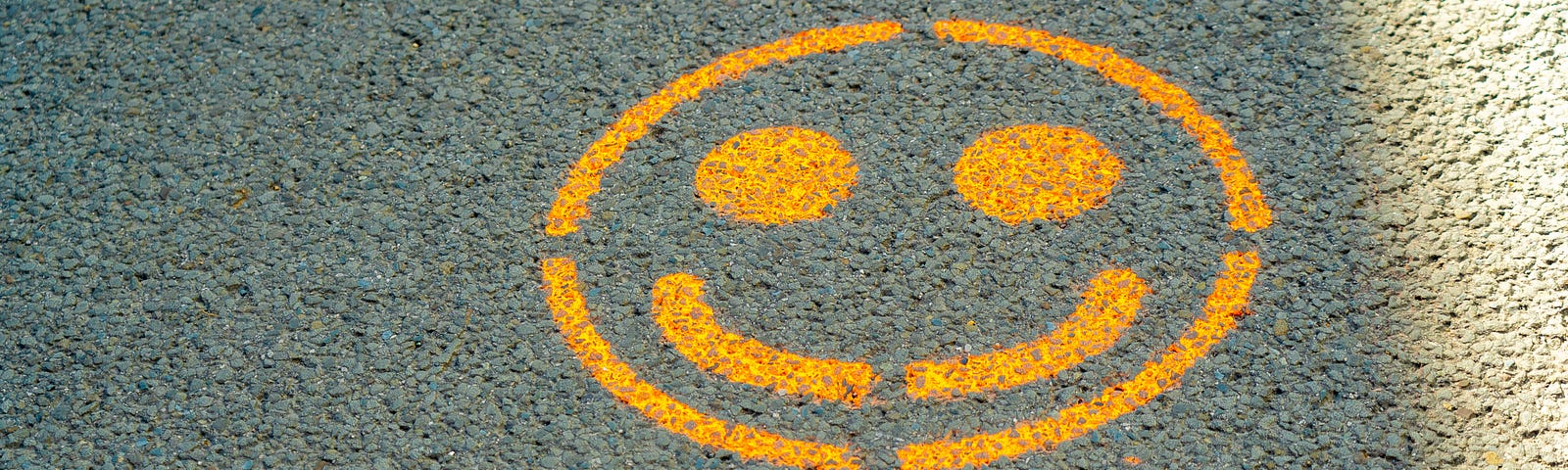 Spray painted on gray pavement are the words “STAY SAFE” in capital letters, colored white. Just above the words, we see a yellow smiley face.