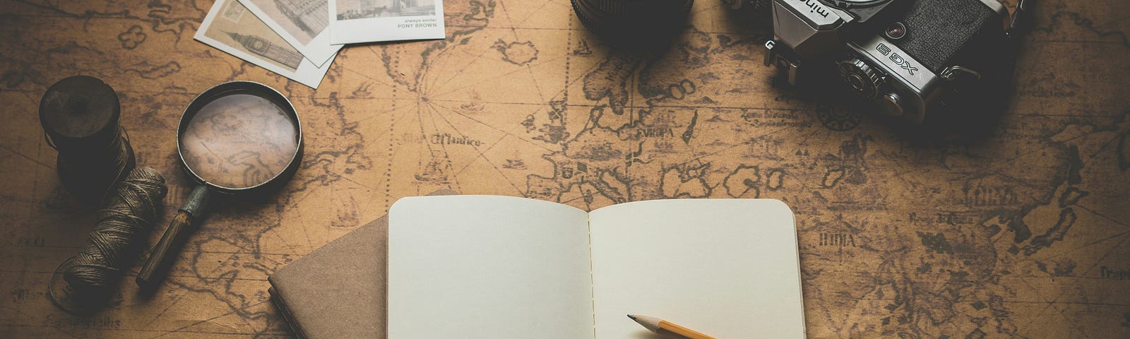 An old map, blank notebook and pencil, a camera, glasses and a magnifying glass