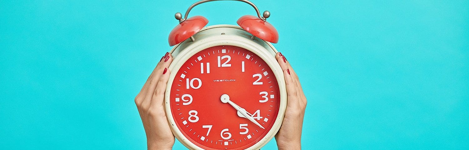 hands holding up orange alarm clock on blue background