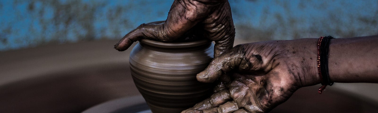 Hands shape clay into a vase on a potter’s wheel