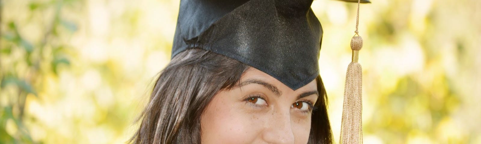 Head shot of female in cap and gown, smiling shyly.