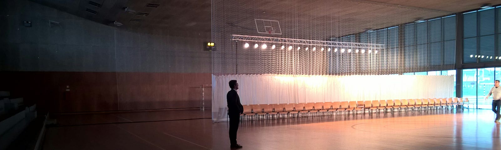 A silhouette of a man is pictured standing in an empty gymnasium that is staged for a performance.