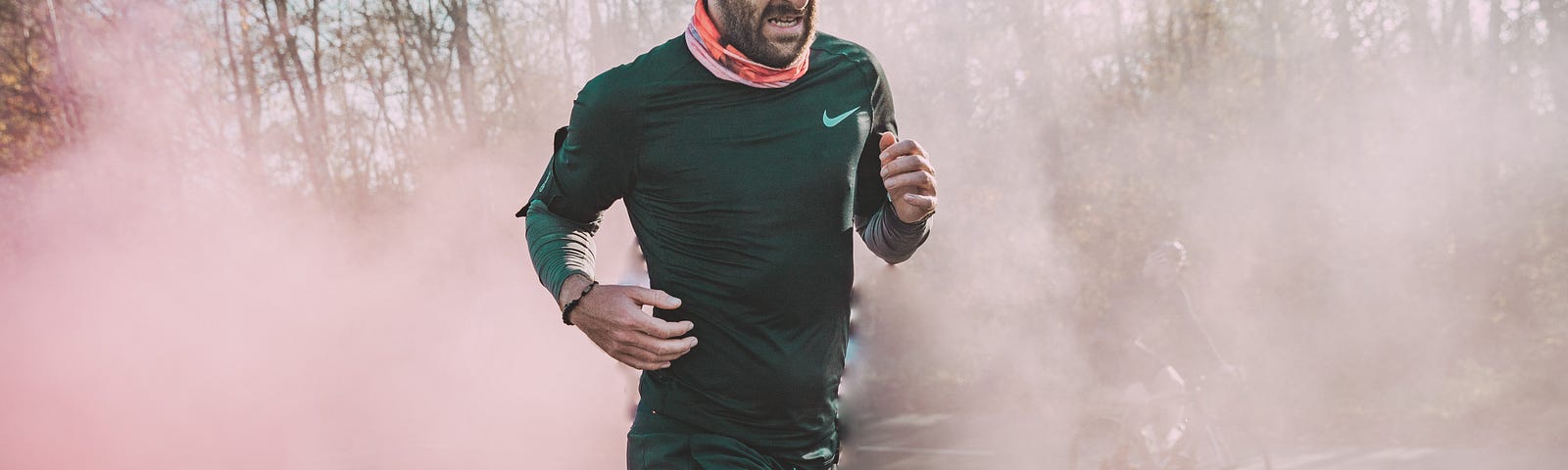 Man running, left to right, with white smoke all around him. Trees are in the distant background.