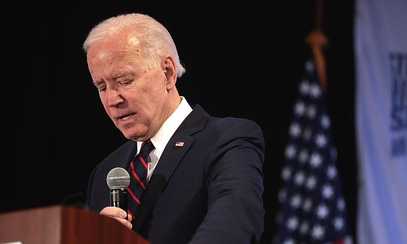 President Biden standing at a podium holding a microphone.