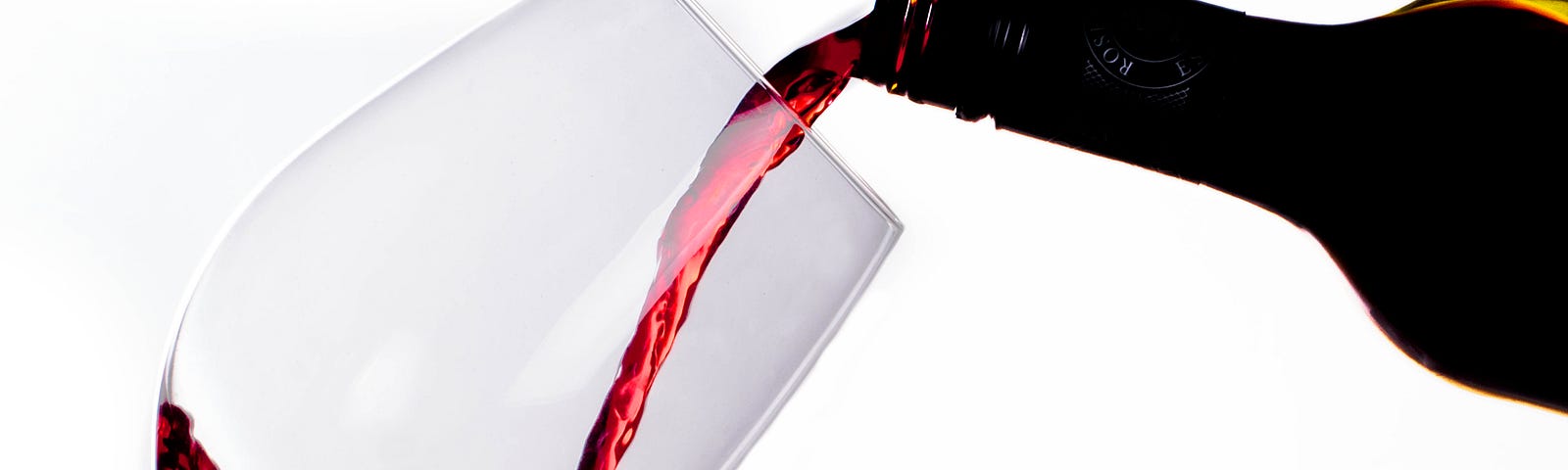 A wine bottle emerges from the right, nearly horizontal to pour red wine into a glass angled (45 degrees) towards the bottle.