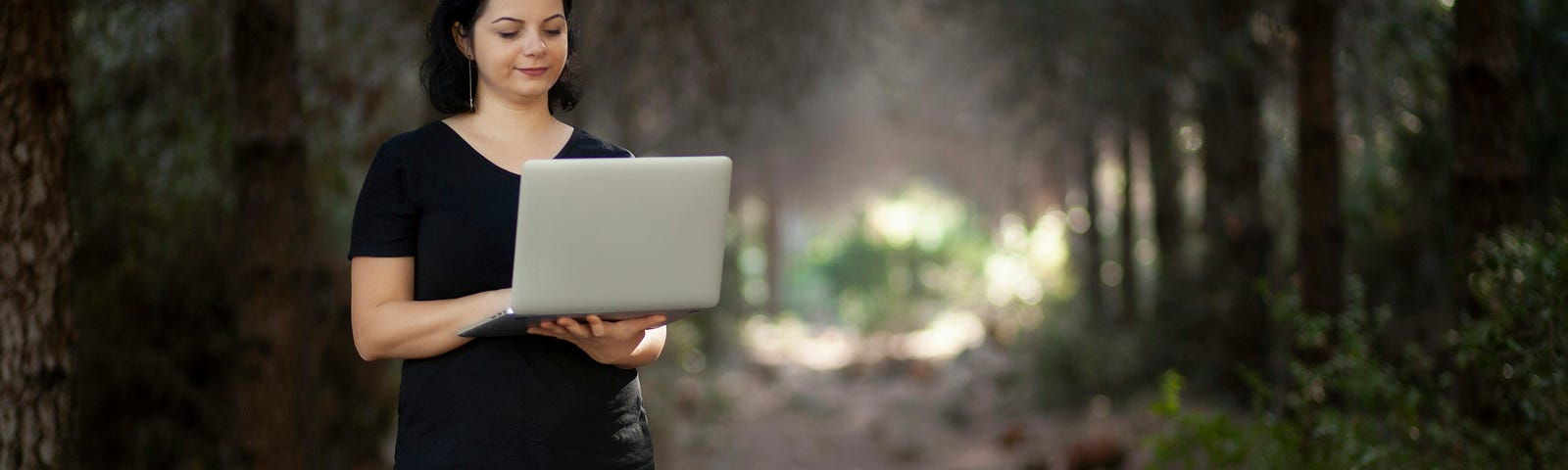 A freelance writer stand in a foggy forest with her laptop open