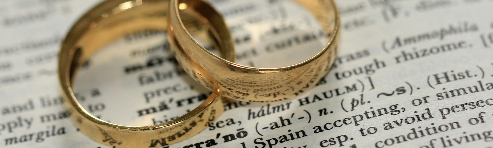 Two wedding rings placed on top of a dictionary page above the definition of marriage