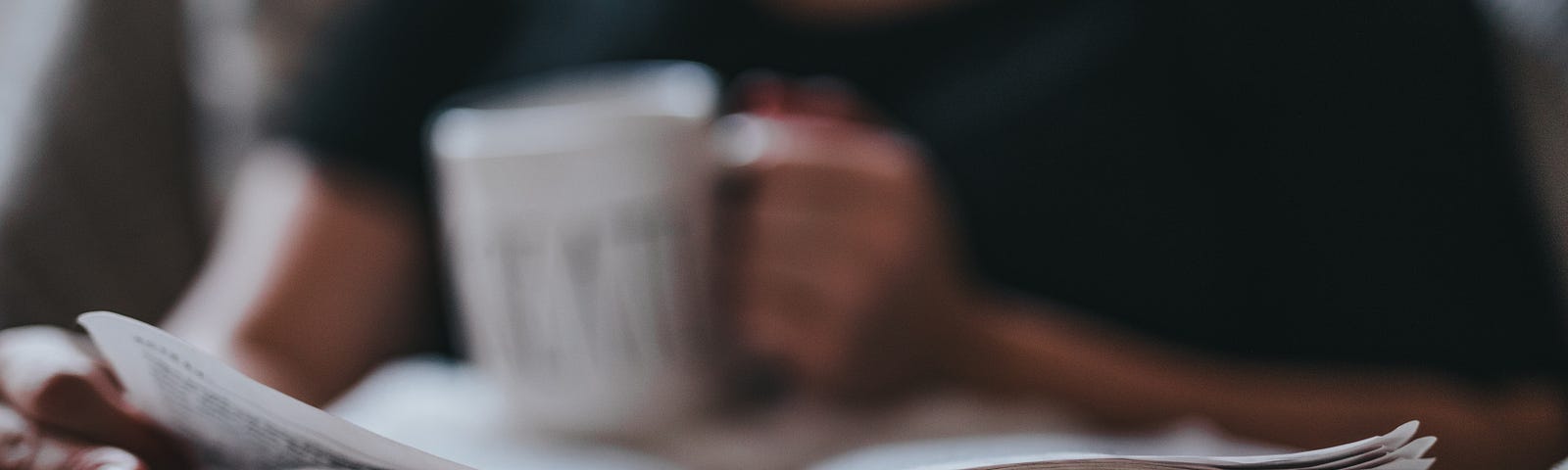 Person reading a book with a cup of coffee in hand.