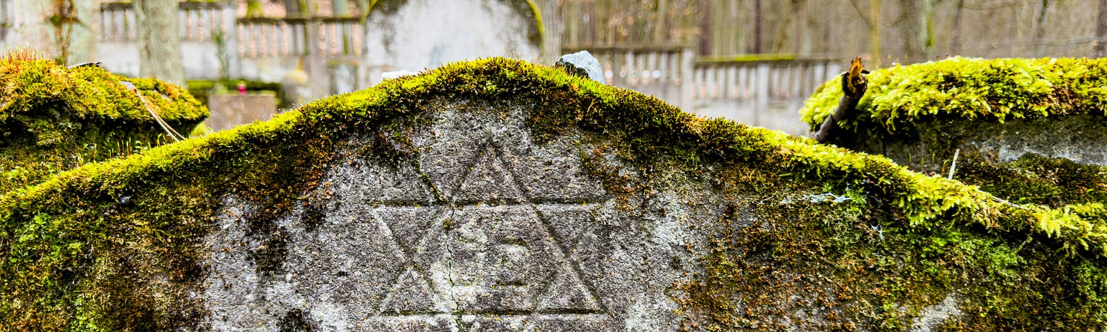 Top of a Jewish headstone, covered in moss, carved with Magen David (Star of David).