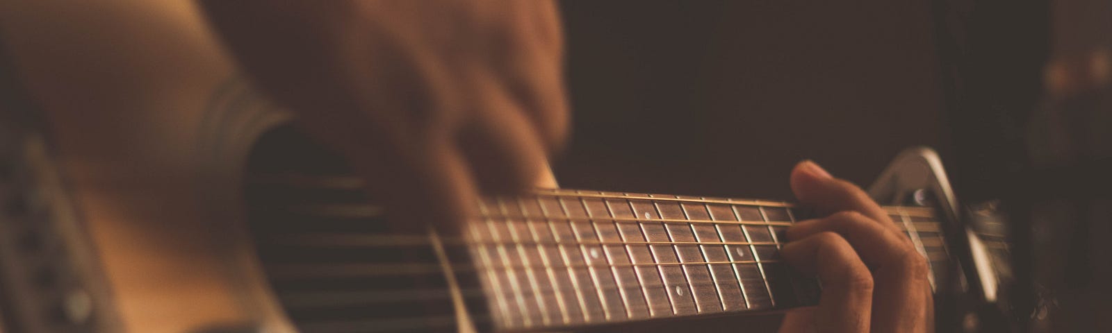 Busy hands play a brown and tan acoustic guitar.