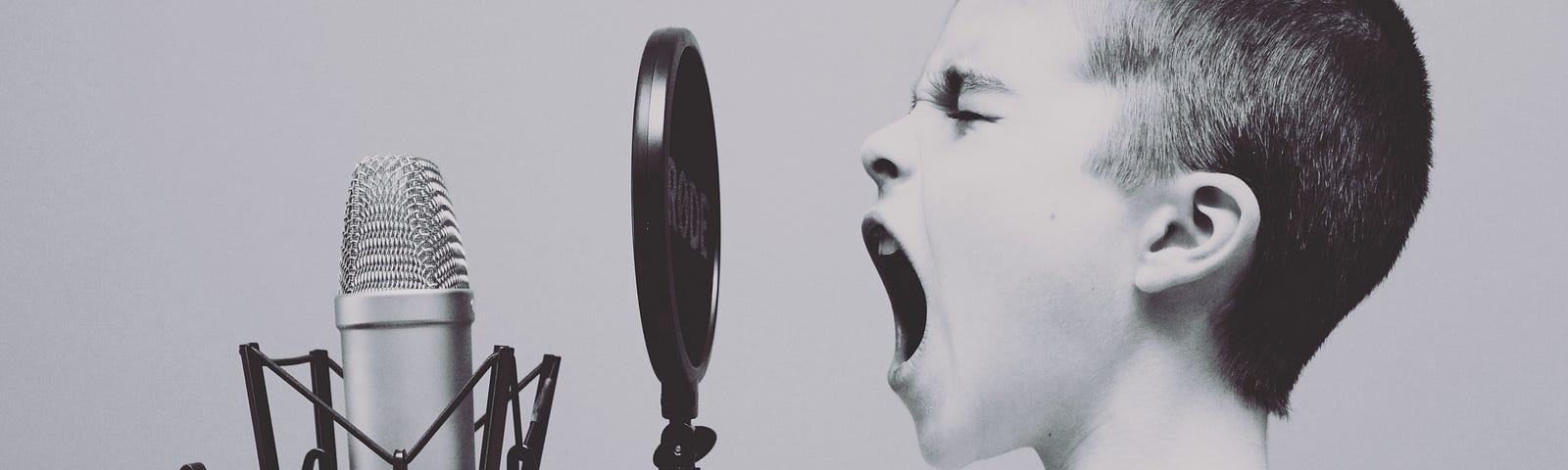 Black and White image of a young boy screaming into a microphone. Technology. Communication. Business