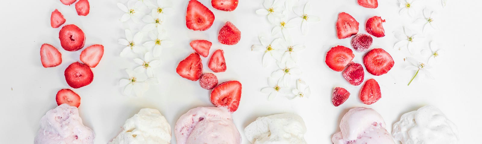 6 icecream cones with alternating strawberry and vanilla icecream, below alternating slived strawberries, and small white flowers