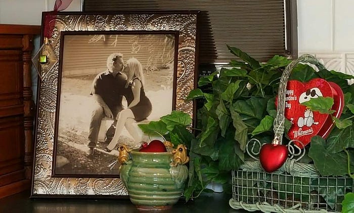 Framed photograph of a couple sitting on a garden bench and kissing, on a counter decorated for Valentine’s Day.