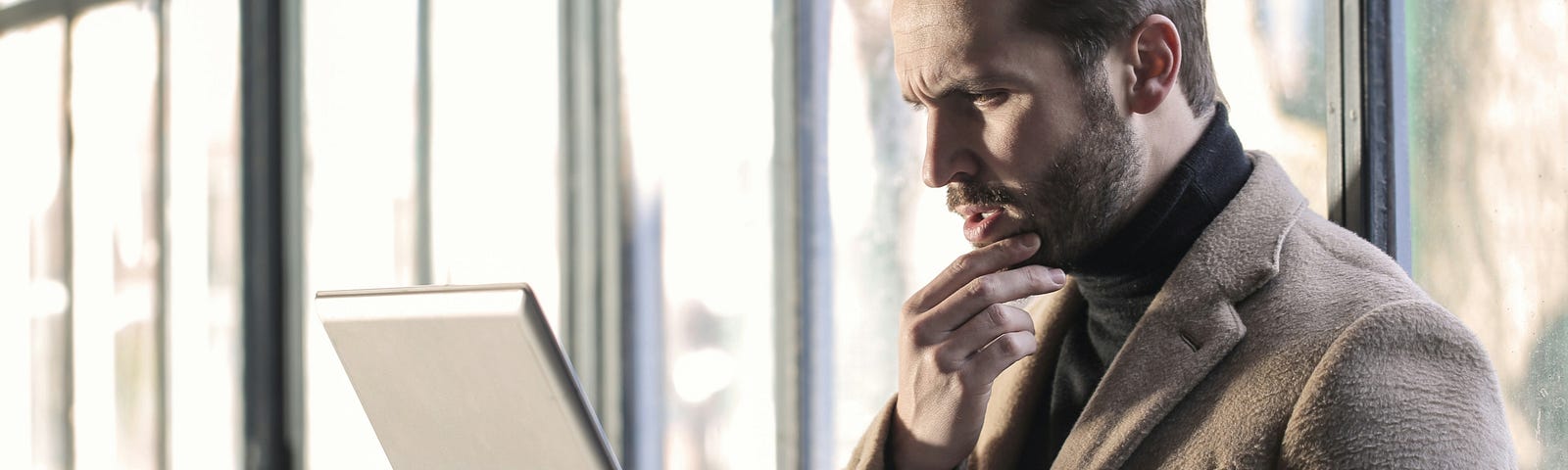 A man looks at his laptop, thinking of his next sentence.