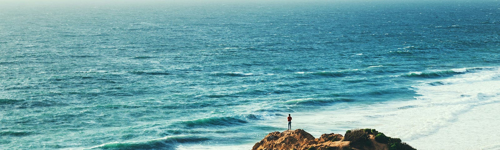Person standing alone on the edge of a cliff, looking out to the ocean