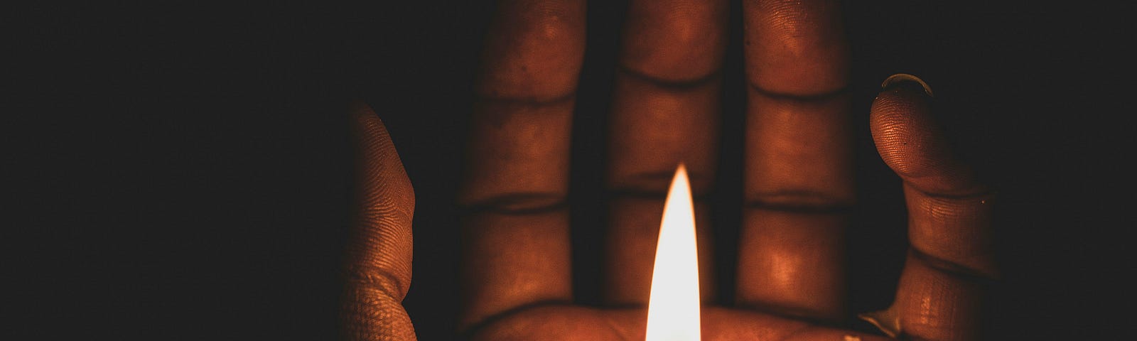 A cupped hand holding a lit candle in the dark