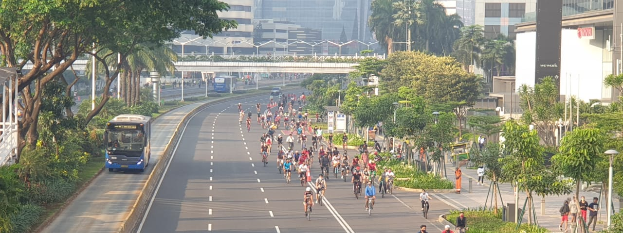 Dozens of cyclists use a wide five-lane road, taking over the street/ A bus is passing by in a protected and separated bus lane.