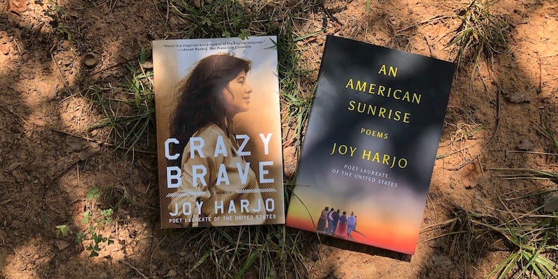 A photo of two books—Crazy Brave and An American Sunrise by Joy Harjo—sitting on the ground.