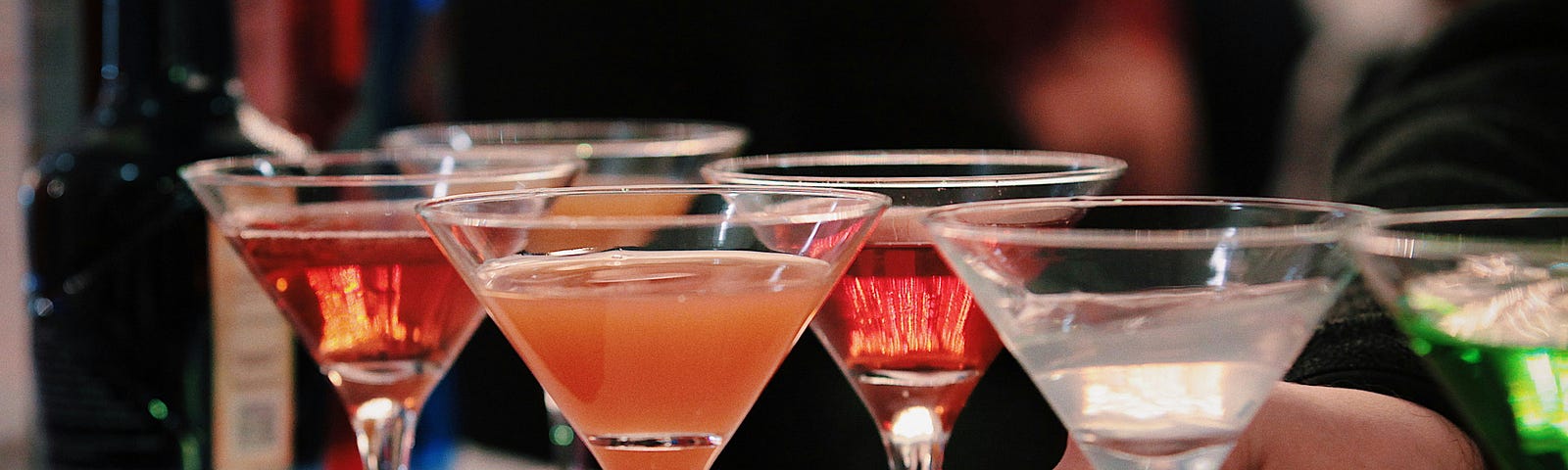 six martini glasses filled with different colored drinks on a bar counter