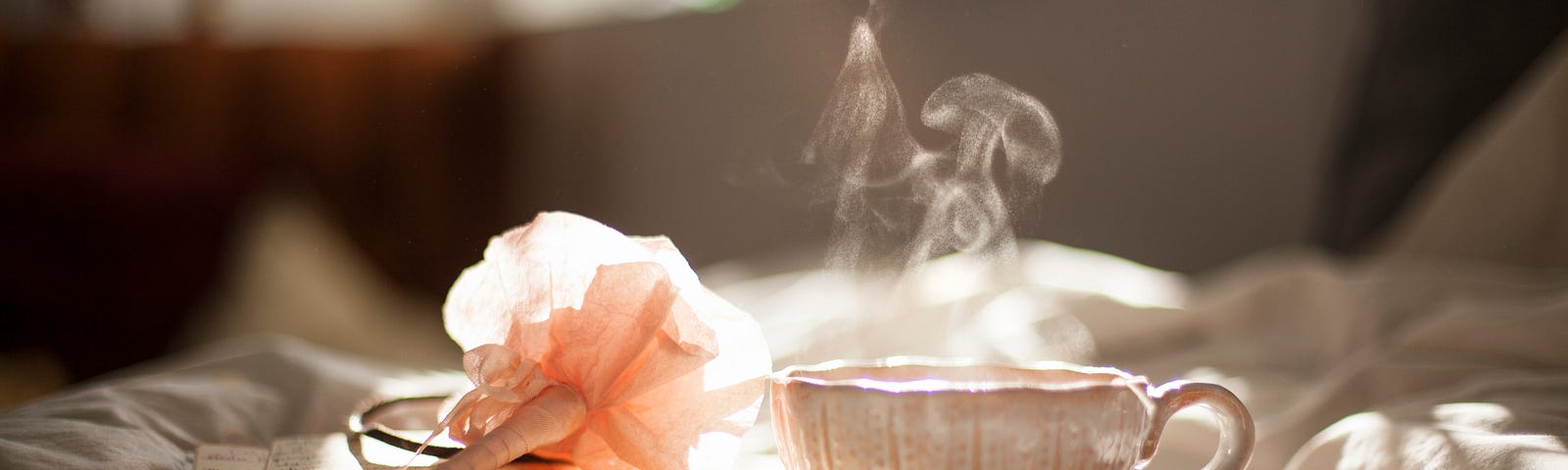 A pen, a book and glass of warm tea place on tablecloth in sunshine