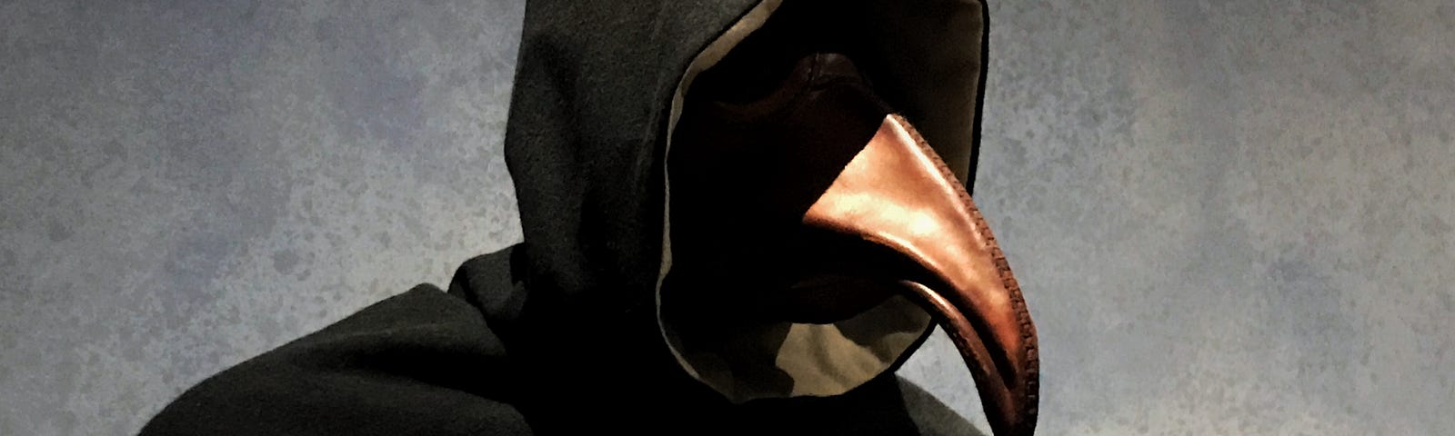 A scary looking figure in a black hood with a beak coming out.