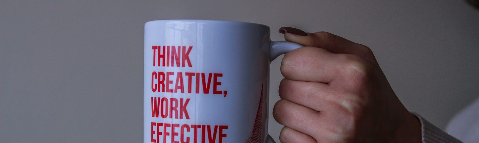 A woman’s hand holding a mug with the message “think creative, work effective”