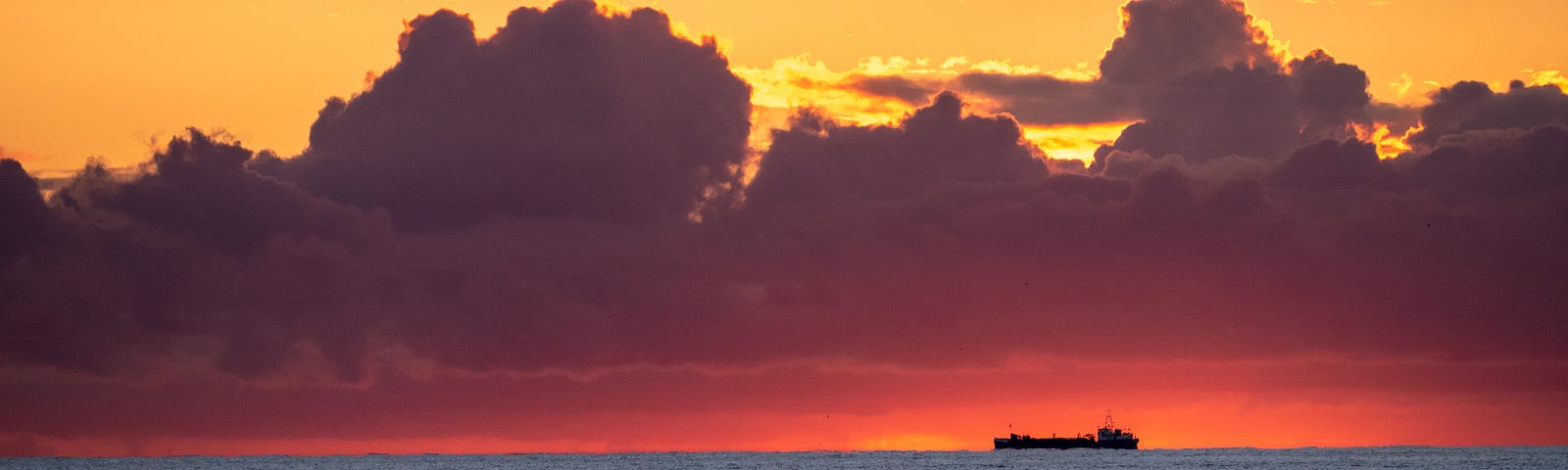 A beautiful horizon with reds and yellows, and a fishing boat just on the edge.