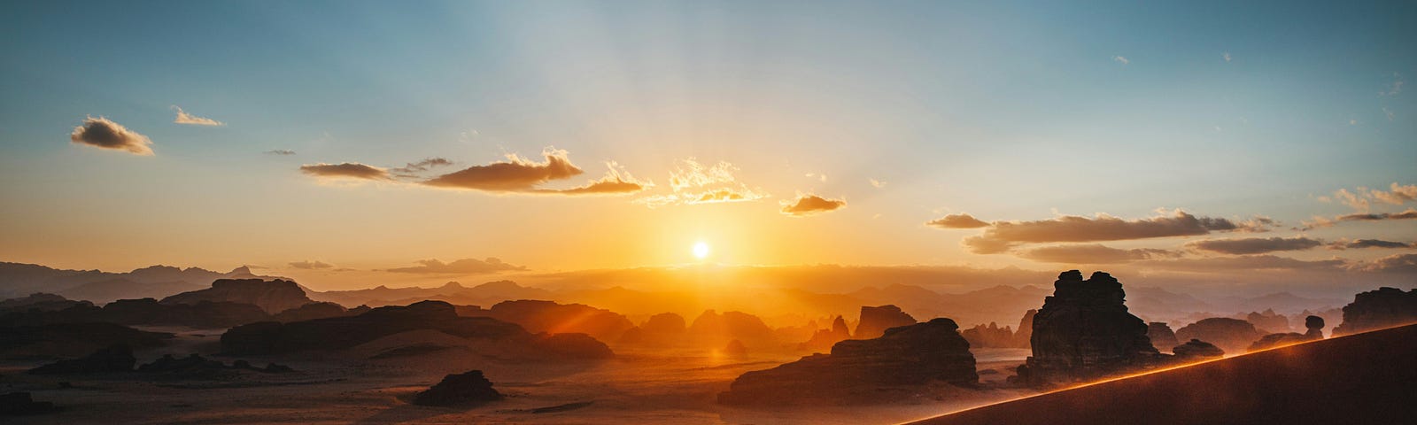 A person in siloette walking up a steep hill in front of a sunrise.