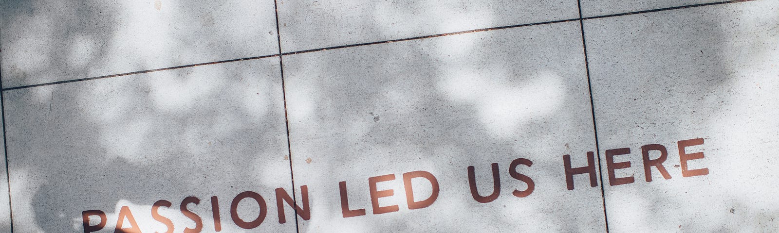 Two pairs of feet standing next to an inscription on the sidewalk which reads, “Passion led us here.”