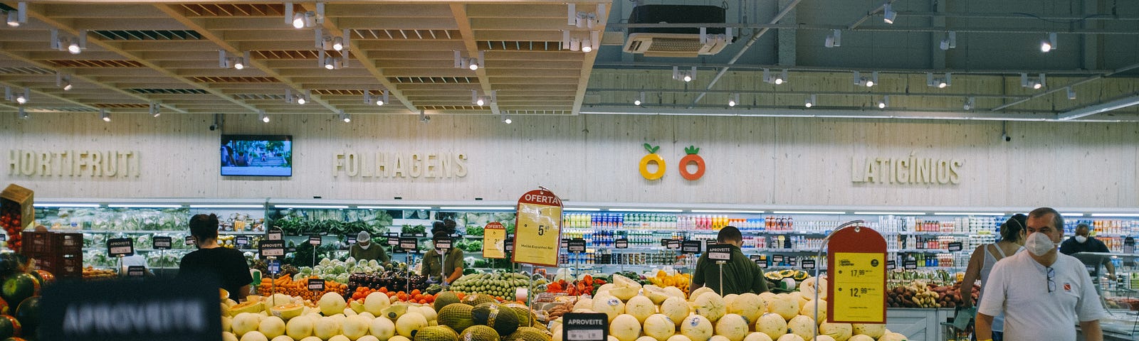 Inside a grocery store with bins of fresh fruit and a few shoppers