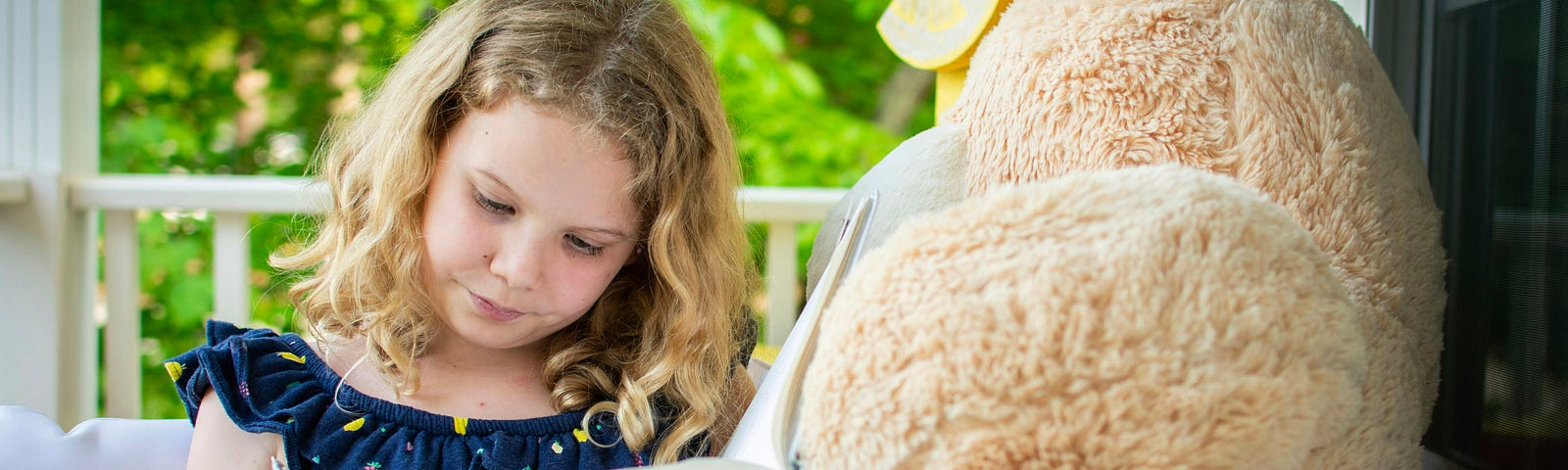 A young girl with a large teddy bear writing in a book