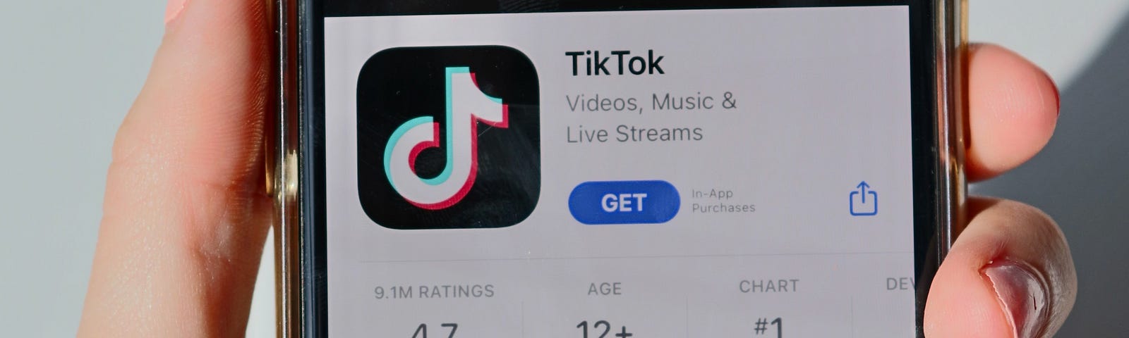 Someone holds up their phone to the camera, showing the home screen of the Tik Tok social media app.
