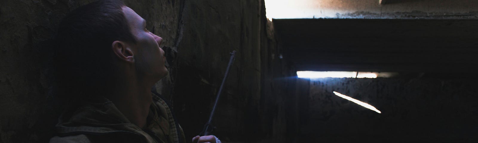 A man with a rifle takes cover behind a barricade.