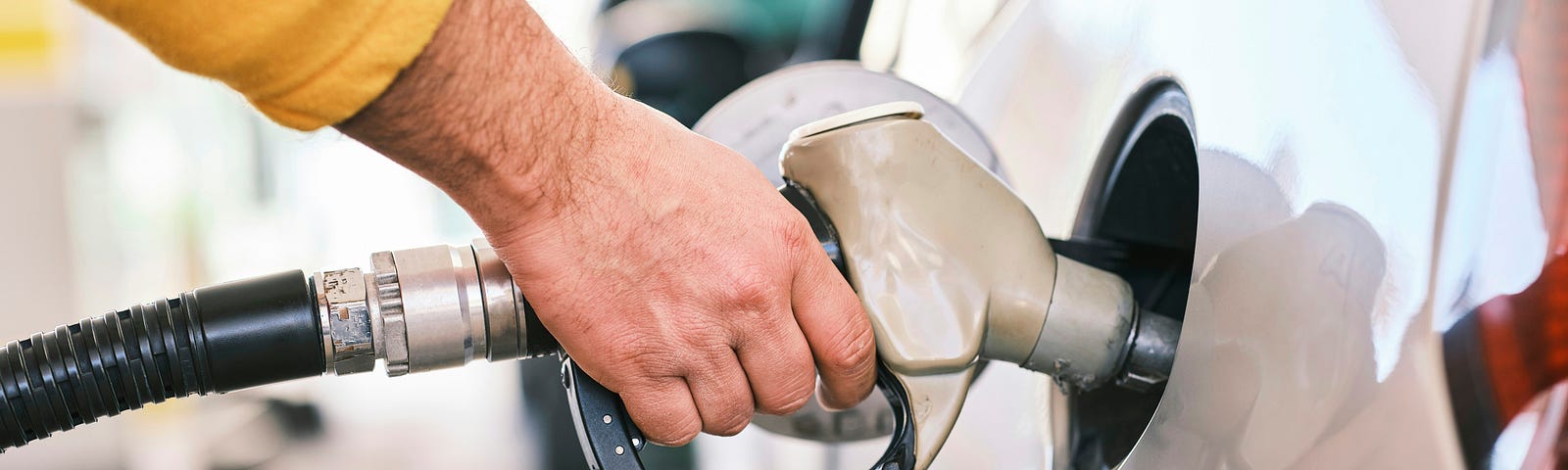 Closeup of a man’s hand holding a gas nozzle, filling a white car with fuel.