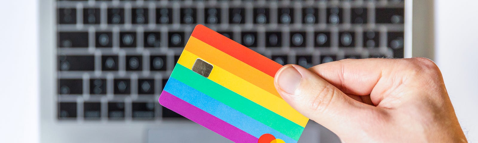 rainbow hued credit card held in front of a keyboard.