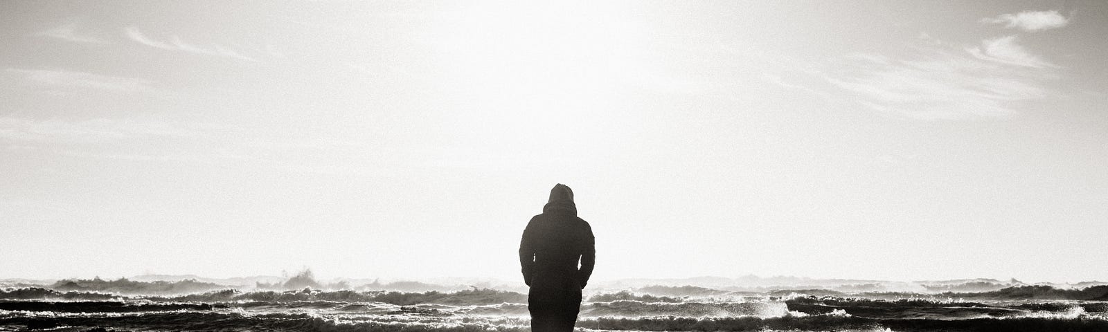 black and white image of a man’s silhouette walking along the shore