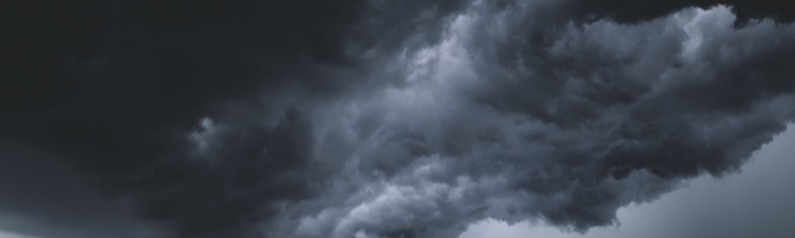 Dramatic roiling storm clouds hovering over a darkened city scape. Forked lightning strikes down upon the buildings below.