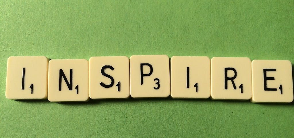Peças do jogo palavra cruzada dispostas sob uma superfície verde, formando a palavra "inspire"
