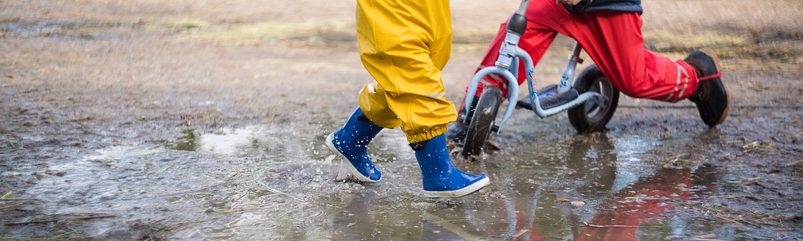 Two children, one jumping in a puddle and one riding a bike through the puddle.